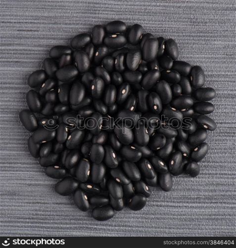 Circle of black beans on grey vinyl background.