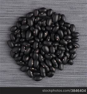 Circle of black beans on grey vinyl background.