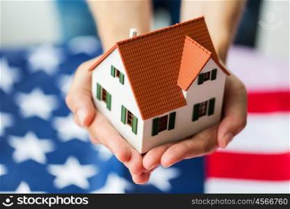 citizenship, residence, property, real estate and people concept - close up of hands holding living house model over american flag