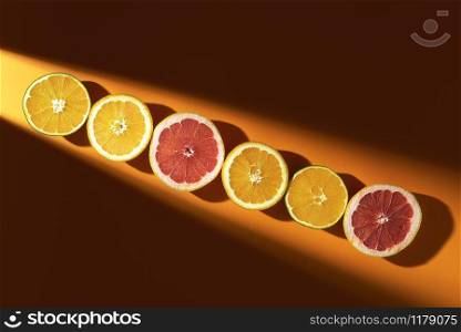 Citrus fruits, cut in half, in a row, in sunlight, on lush lava colored background. Above view of summer tropical fruits. Fresh oranges and grapefruit