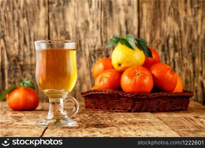 Citrus tea in a glass cup, warm healthy drink in the cool seasonon, background of mandarin and lemon fruits piled in a wicker basket on an old wooden table in blur, copy space.. Citrus tea in a glass cup on a background of mandarin and lemon fruits in blur.