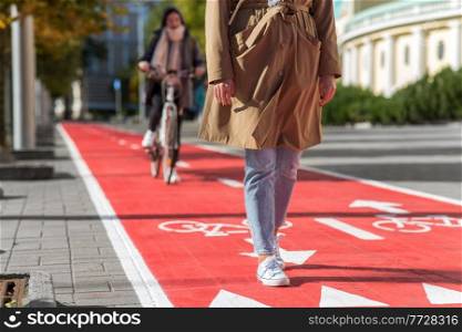 city and traffic concept - close up of woman walking along separate bike lane or red road with signs only for bicycles on street. woman walking along bike lane or road for bicycles