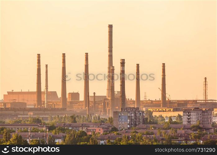 City buildings on the background of steel factory with smokestacks at colorful sunset. metallurgical plant. steelworks, iron works. Heavy industry in Europe. Air pollution from smokestacks. Industrial landscape