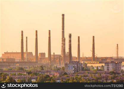 City buildings on the background of steel factory with smokestacks at colorful sunset. metallurgical plant. steelworks, iron works. Heavy industry in Europe. Air pollution from smokestacks. Industrial landscape