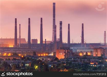City buildings on the background of steel factory with smokestacks at night. Metallurgical plant with chimney. steelworks, iron works. Heavy industry. Air pollution, smog. Industrial landscape