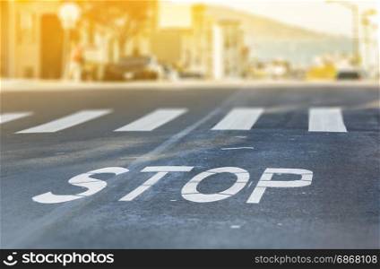 City crosswalk with symbol stop, closeup road texture with blurred San Francisco Bay in background in a warm sunny day
