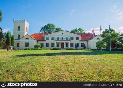 City Dzerbene, Latvia. Old manor house and meadow, green trees. Travel photo 2018.