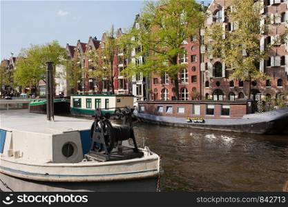 City of Amsterdam, barges and houseboats on a canal and historic apartment buildings (former warehouses), Holland, Netherlands.