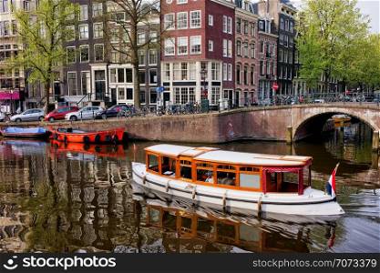 City of Amsterdam in Holland picturesque scenery, boats on a canal and historic terraced houses.