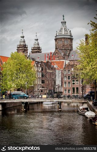 City of Amsterdam in Netherlands, bridge, canal, historic buildings and towers of Saint Nicholas Church in the background.