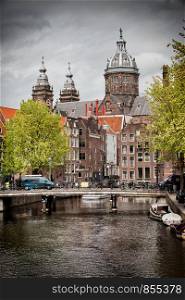 City of Amsterdam in Netherlands, bridge, canal, historic buildings and towers of Saint Nicholas Church in the background.