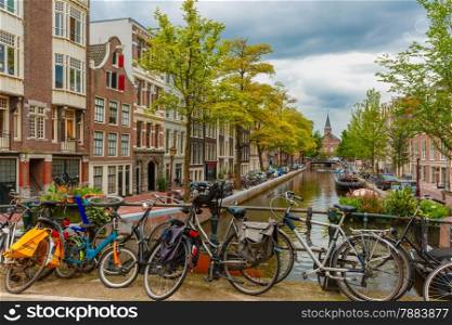 City view of Amsterdam canal and bridge with bikes, typical houses, church and boats, Holland, Netherlands.