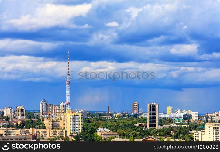 Cityscape of the summer city of Kyiv with a television tower and residential quarters in the impending thunderclouds on the horizon.. TV tower and residential areas of Kyiv at noon against the backdrop of a stormy blue summer sky.