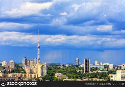 Cityscape of the summer city of Kyiv with a television tower and residential quarters in the impending thunderclouds on the horizon.. TV tower and residential areas of Kyiv at noon against the backdrop of a stormy blue summer sky.