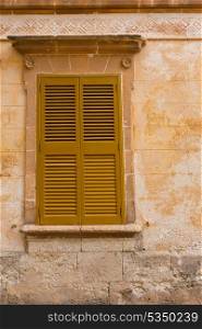 Ciutadella Menorca wooden shutter window on grunge yellow downtown wall at Balearic islands