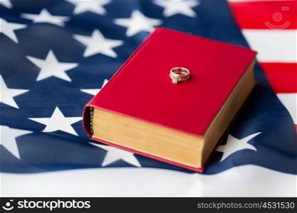civil rights, family values and marriage concept - close up of american flag and wedding rings on book or bible