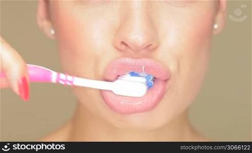 Claoseup of the face of a beautiful woman with her lips parted holding a toothbrush topped with striped toothpaste