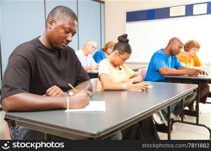 Class of adult college students taking a test. Focus on guy in front left.