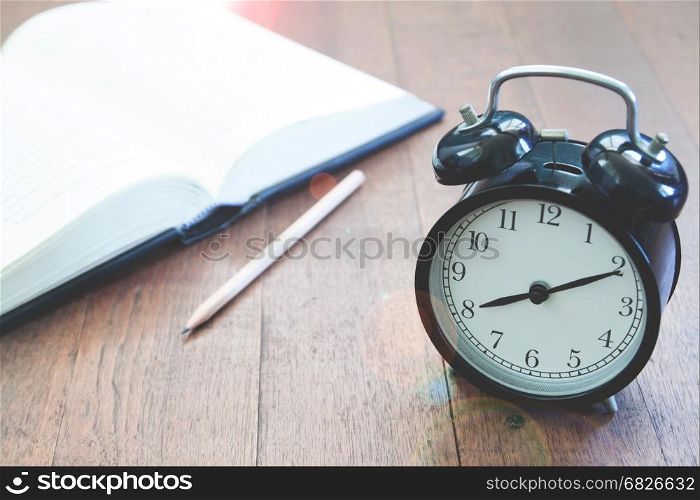 Classic alarm clock with book on wooden background