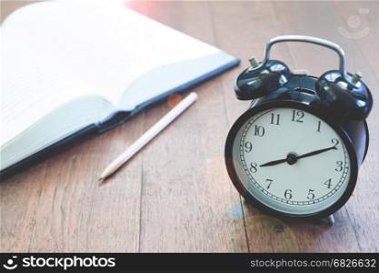 Classic alarm clock with book on wooden background