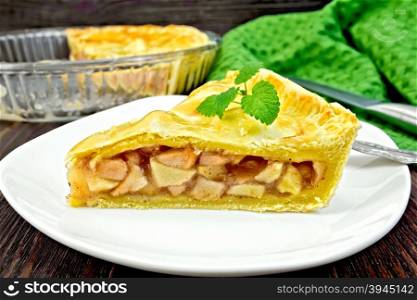 Classic American apple pie with mint leaves in a plate, a napkin, a pie in a glass form on a wooden boards background