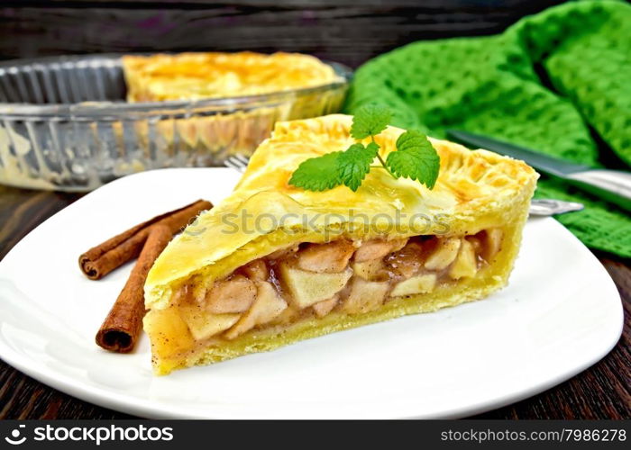 Classic American apple pie with whipped cream in a plate with cinnamon, napkin, a pie in a glass form on a wooden boards background