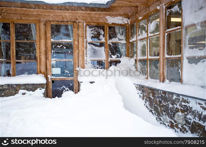 Classic Austrian wooden house with big windows covered by snow at snowstorm