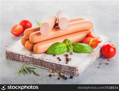 Classic boiled meat pork sausages on chopping board with pepper and basil and cherry tomatoes on light background. Snack for kids