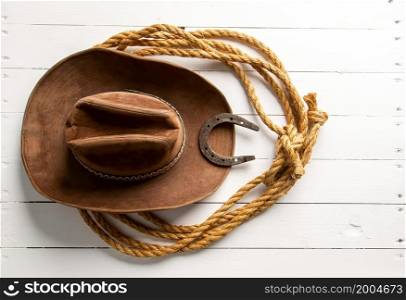 Classic brown cowboy hat lasso and horseshoe wild west still life on rough white wooden table