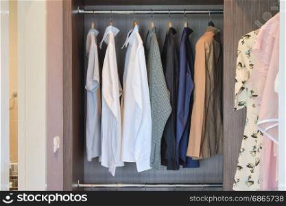 Classic color shirts are hanging in open wooden wardrobe