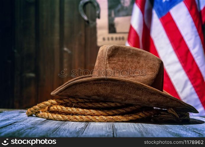 Classic cowboy hat and lasso lie on a wooden table against the background of the US flag and the poster for the search for the criminal in the sheriff&rsquo;s office