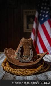 Classic cowboy hat and lasso lie on a wooden table against the background of the US flag and the poster for the search for the criminal in the sheriff&rsquo;s office