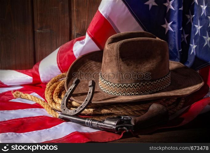 Classic cowboy hat lasso and horseshoe lie on a star-striped USA flag on a dark wooden background. Flag Hat and Horseshoe