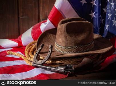 Classic cowboy hat lasso and horseshoe lie on a star-striped USA flag on a dark wooden background. Flag Hat and Horseshoe