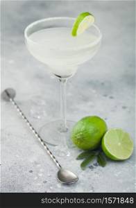 Classic crystal glass of Margarita cocktail with fresh lime and bar spoon on light table background