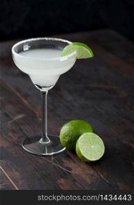 Classic glass of Margarita cocktail with fresh limes on wooden table background.