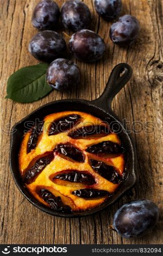 Classic golden cast iron pie and fresh purple plum on the rustic wooden background
