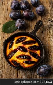 Classic golden cast iron pie and fresh purple plum on the rustic wooden background