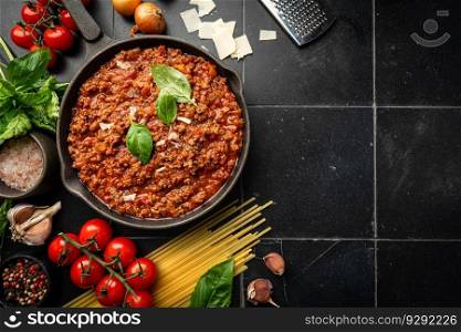 classic italian bolognese sauce stewed in a pan with ingredients on black tile background, top view. classic italian bolognese sauce