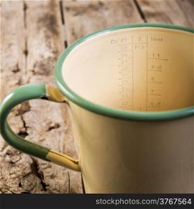 Classic old measuring jug in vintage colours in shallow focus on a wooden table