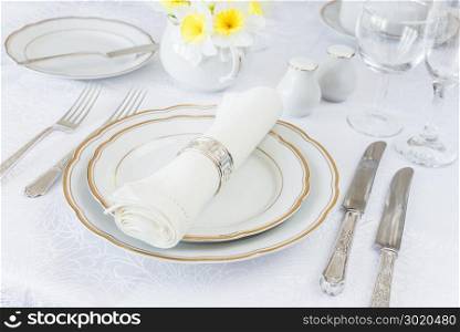 Classic serving for a gala dinner with luxurious porcelain, silverware and spring flowers on a white tablecloth