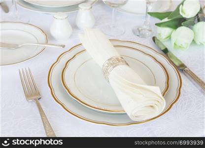 Classic serving for a gala dinner with luxurious porcelain, silverware and tulip flowers on a white tablecloth