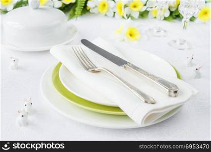 Classic serving for a gala dinner with white and green porcelain plates, silverware and spring flowers on a white tablecloth