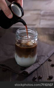 Classic still life with The hand is pouring milk to a glass bottle of coffee with copy space, verticle vintage picture.