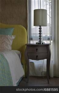 Classic style bedside table with reading lamp next to cozy style bedding with many style of green and yellow pillows