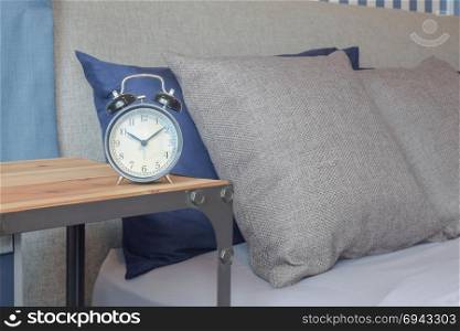 Classic style clock on wooden table next to brown color bedding