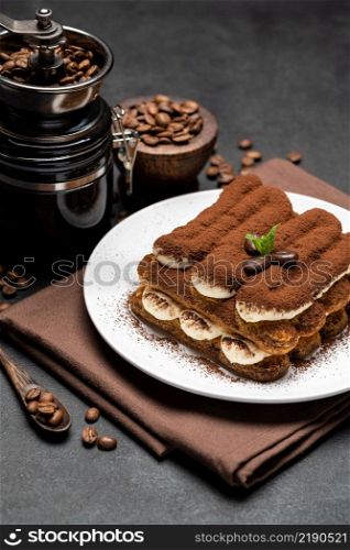 Classic tiramisu dessert and coffee grinder on ceramic plate on concrete background or table. Classic tiramisu dessert and coffee grinder on ceramic plate on concrete background