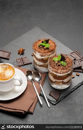 Classic tiramisu dessert in a glass and cup of coffee on dark concrete background or table. Classic tiramisu dessert in a glass and cup of coffee on dark concrete background