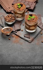 Classic tiramisu dessert in a glass and pieces of chocolate on dark concrete background or table. Classic tiramisu dessert in a glass and pieces of chocolate on dark concrete background