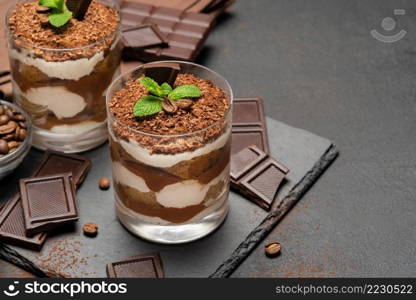 Classic tiramisu dessert in a glass and pieces of chocolate on dark concrete background or table. Classic tiramisu dessert in a glass and pieces of chocolate on dark concrete background